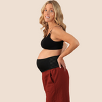 A pregnant woman wearing a black maternity support belt with red pants.