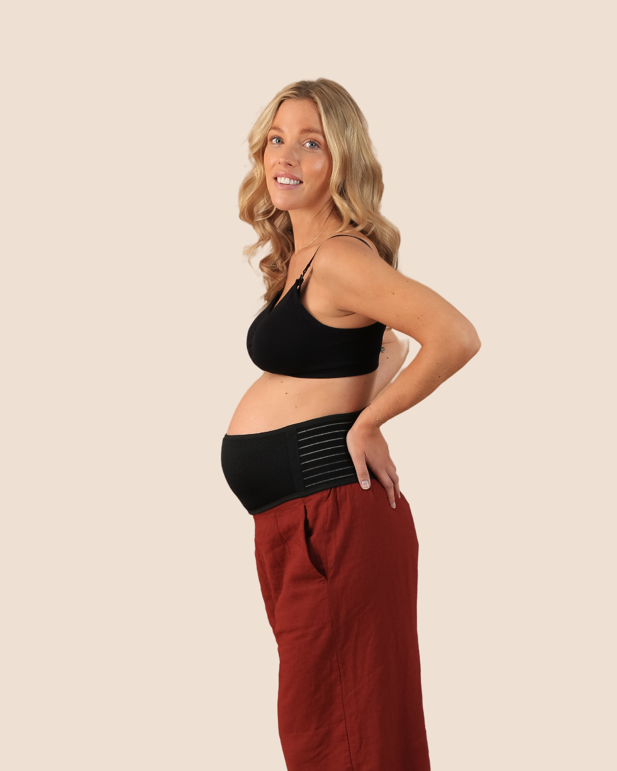 A pregnant woman wearing a black maternity support belt with red pants.