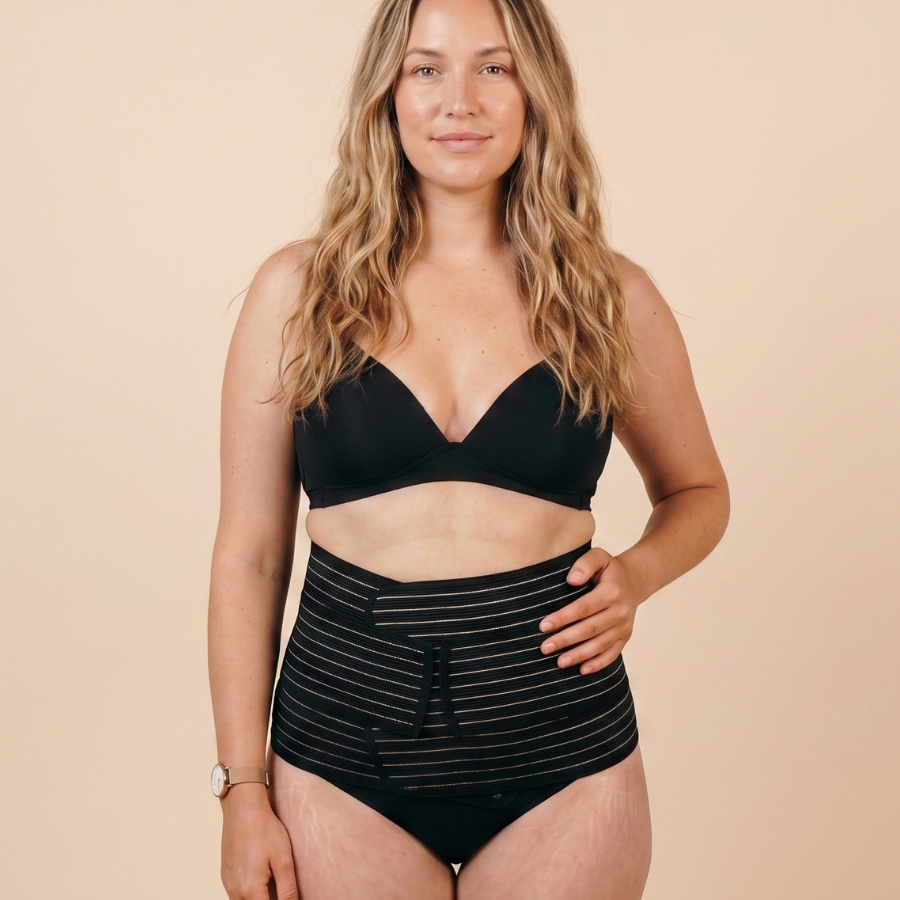 Woman wearing the black MammaBump Postpartum Belly Band against a warm neutral background.