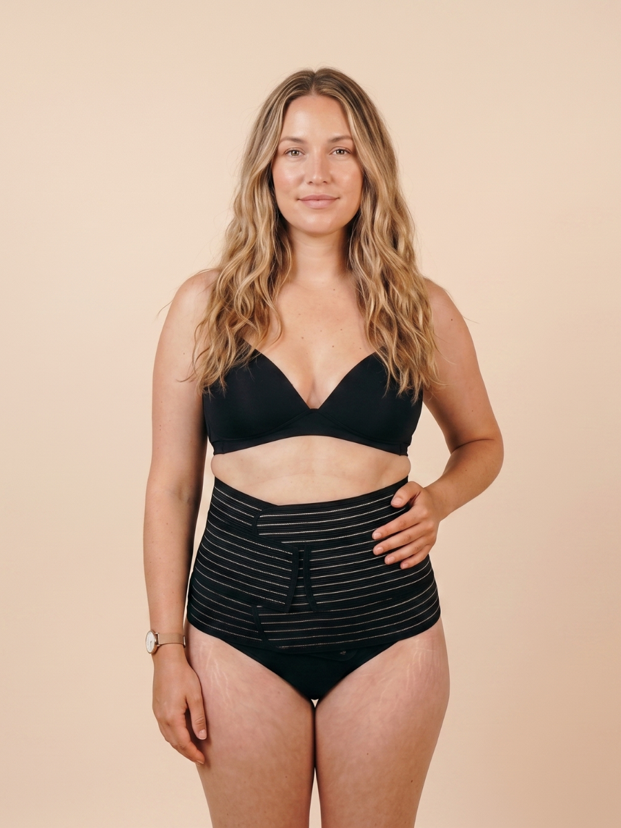Woman wearing the black MammaBump Postpartum Belly Band against a warm neutral background.