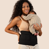 New mum holding her sleeping baby while wearing the black MammaBump Postpartum Belly Band, a quiet moment of postpartum recovery