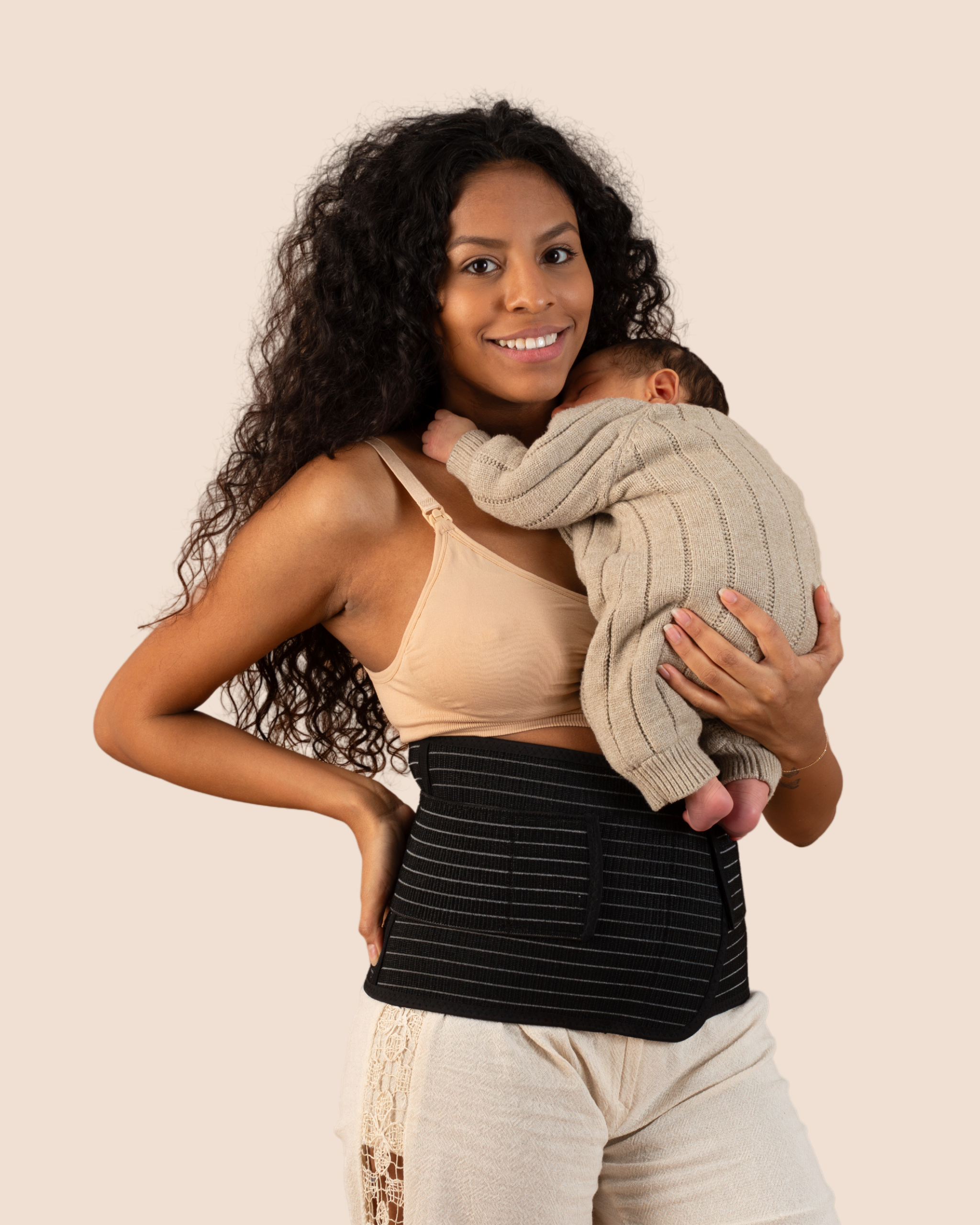New mum holding her sleeping baby while wearing the black MammaBump Postpartum Belly Band, a quiet moment of postpartum recovery