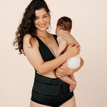 Smiling new mum holding her baby while wearing the black MammaBump Postpartum Belly Band for gentle support during postpartum recovery