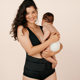 Smiling new mum holding her baby while wearing the black MammaBump Postpartum Belly Band for gentle support during postpartum recovery