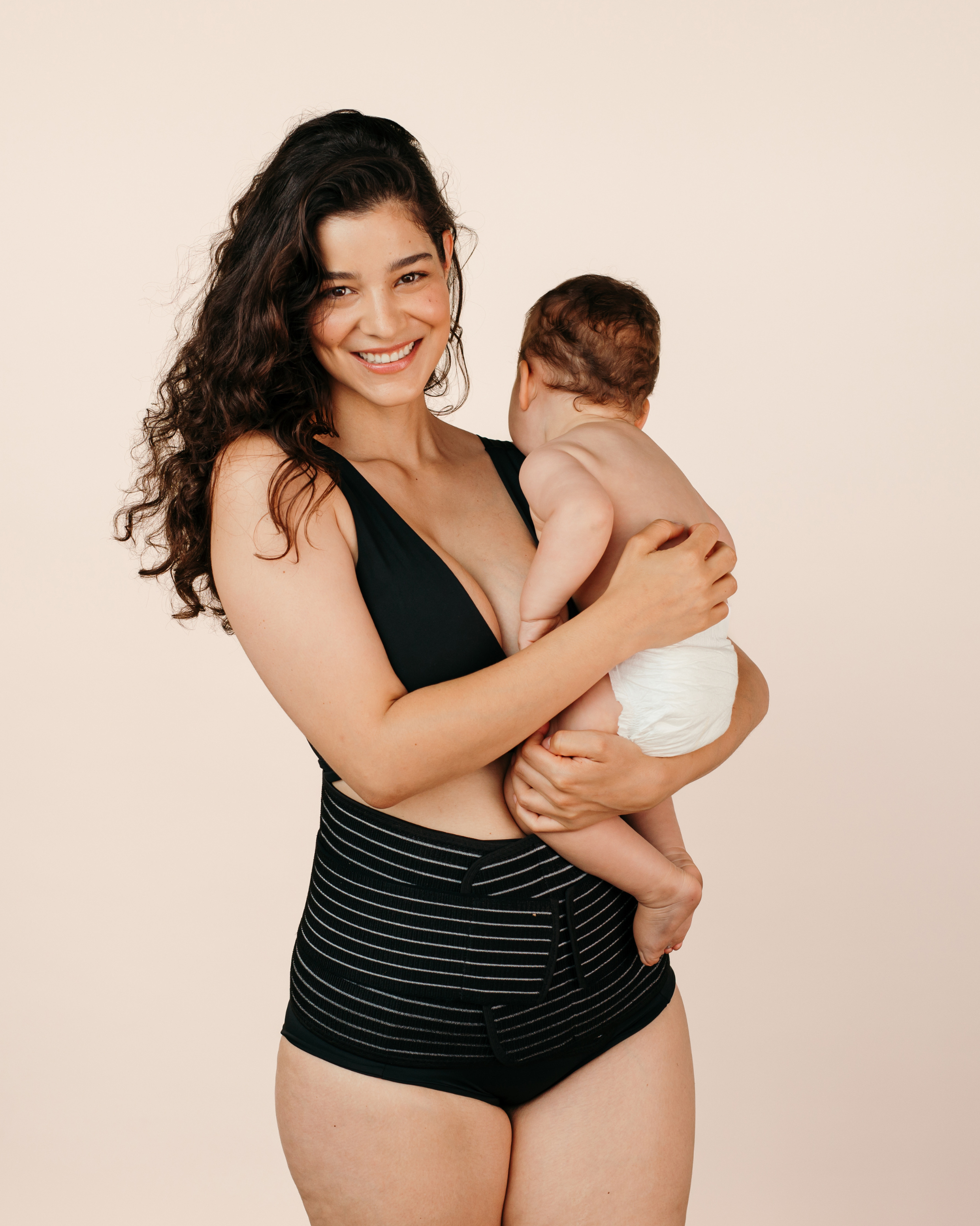 Smiling new mum holding her baby while wearing the black MammaBump Postpartum Belly Band for gentle support during postpartum recovery