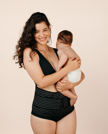 New mum holding her baby confidently while wearing the black MammaBump Postpartum Belly Band, showing real postpartum life and recovery