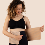 New mum wrapping the tan MammaBump Postpartum Belly Band around her waist for gentle postpartum recovery support after vaginal birth