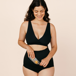 Smiling new mum placing the MammaBump Perineal Hot & Cold Therapy Pack into her black Postpartum Soothing Brief for soothing perineal relief