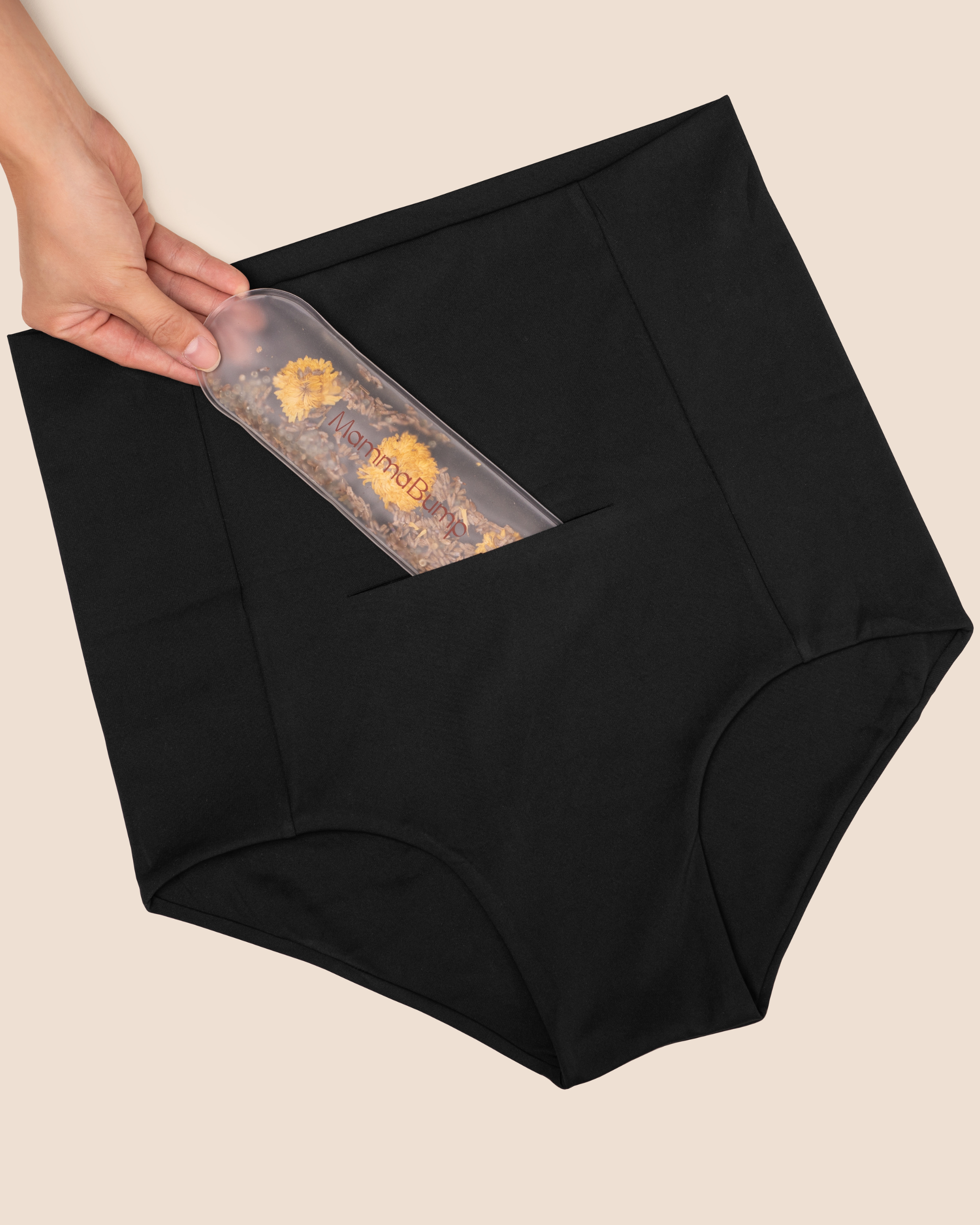 Hand inserting the MammaBump Perineal Hot & Cold Therapy Pack into the front pocket of the black Postpartum Soothing Brief for targeted relief