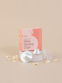 A boxed set of silver nursing cups, silverettes, displayed on a pedestal with two cups and a clear lid in front of a peach and pink box. The box reads 'Breastfeeding Aids Silver Nursing Cups' and 'Alarmed Bump!'.